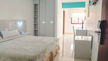 Una habitación de hotel con cama, escritorio, armario y ventana con cortinas.