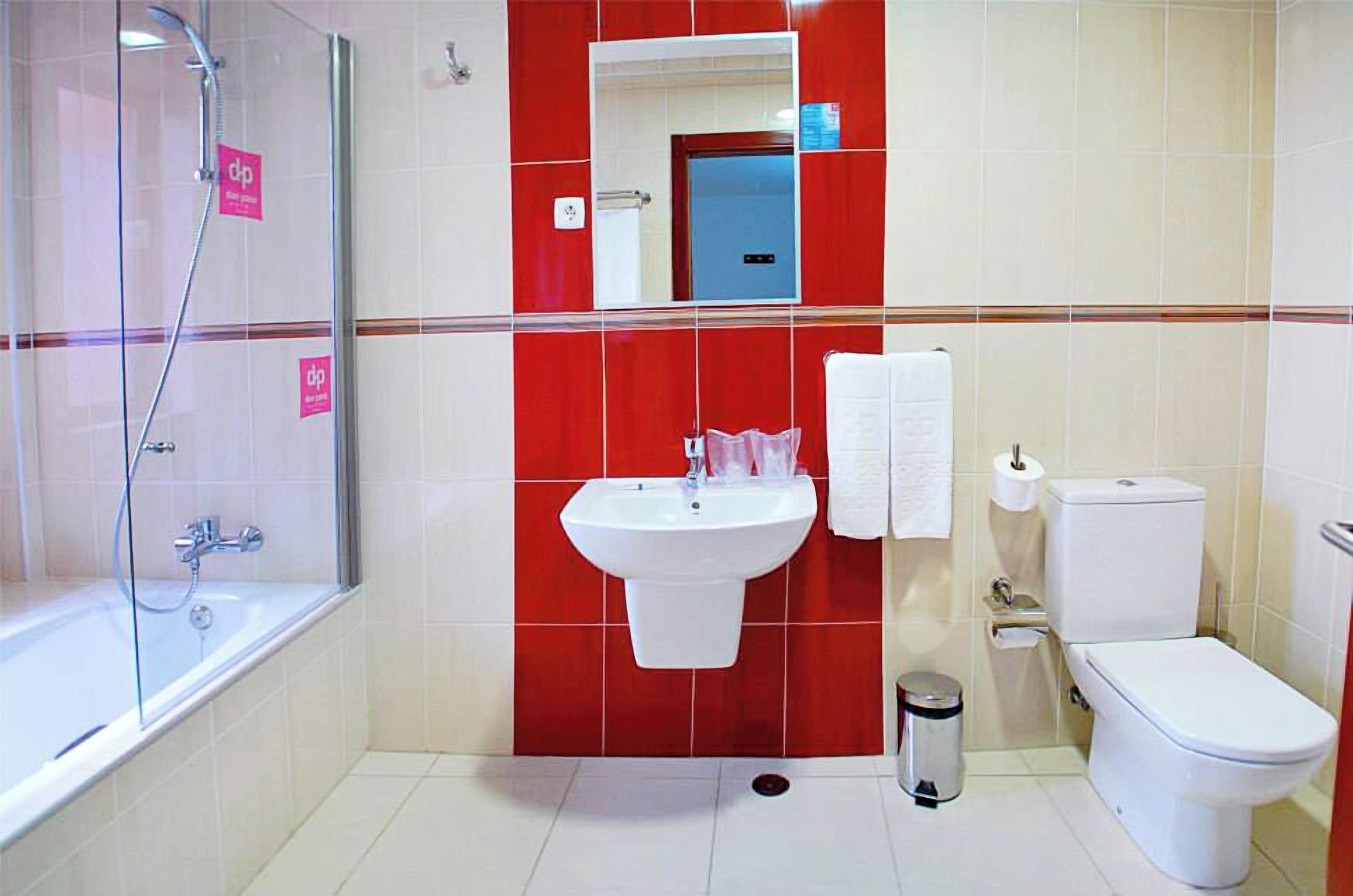 A bathroom with a shower, sink, toilet, and a mirror.
