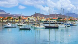 Una marina amb diverses embarcacions amarrades, envoltada d'edificis de colors i muntanyes al fons.