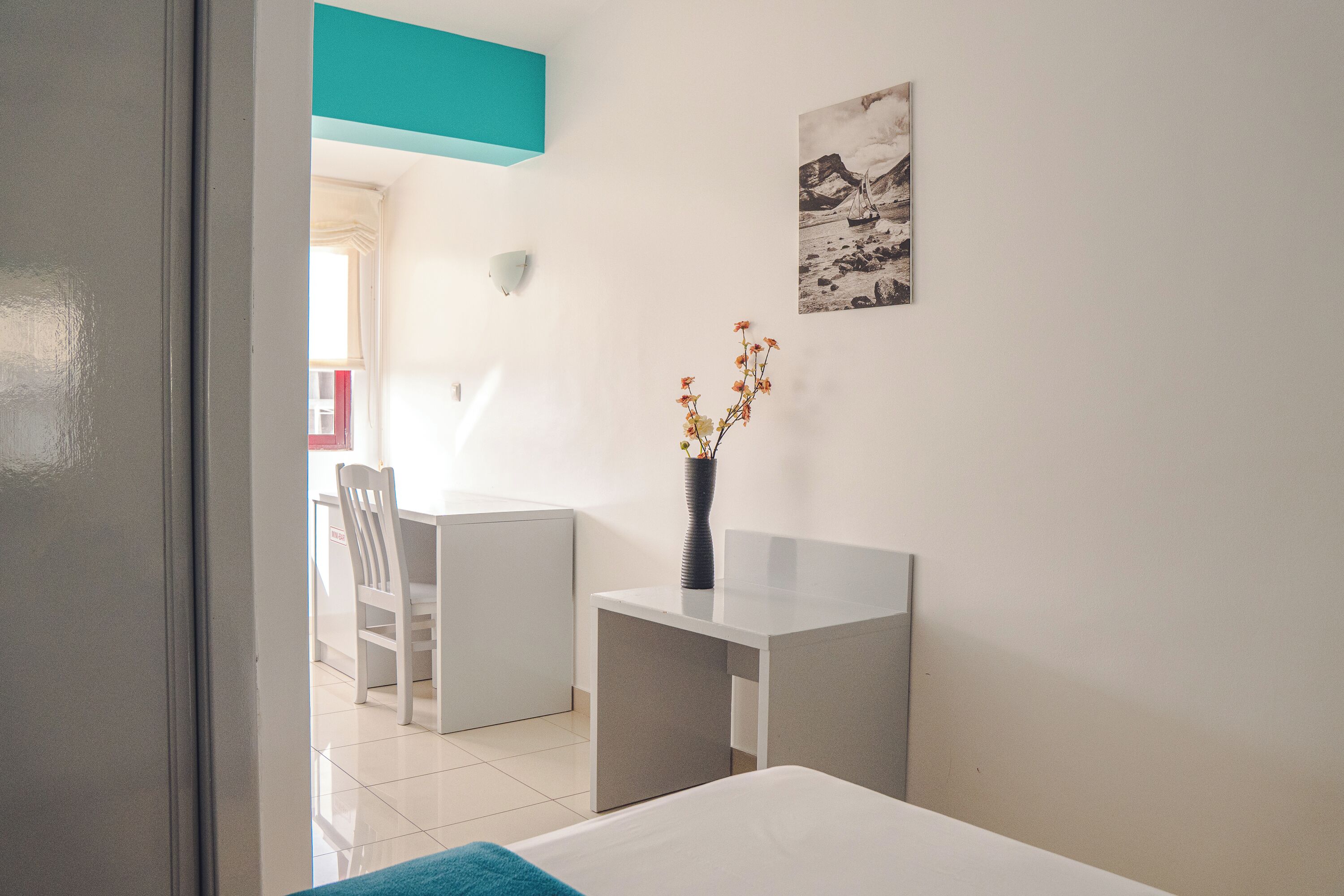Una habitación moderna con una cama, un escritorio y una silla. Hay un florero con flores sobre el escritorio.