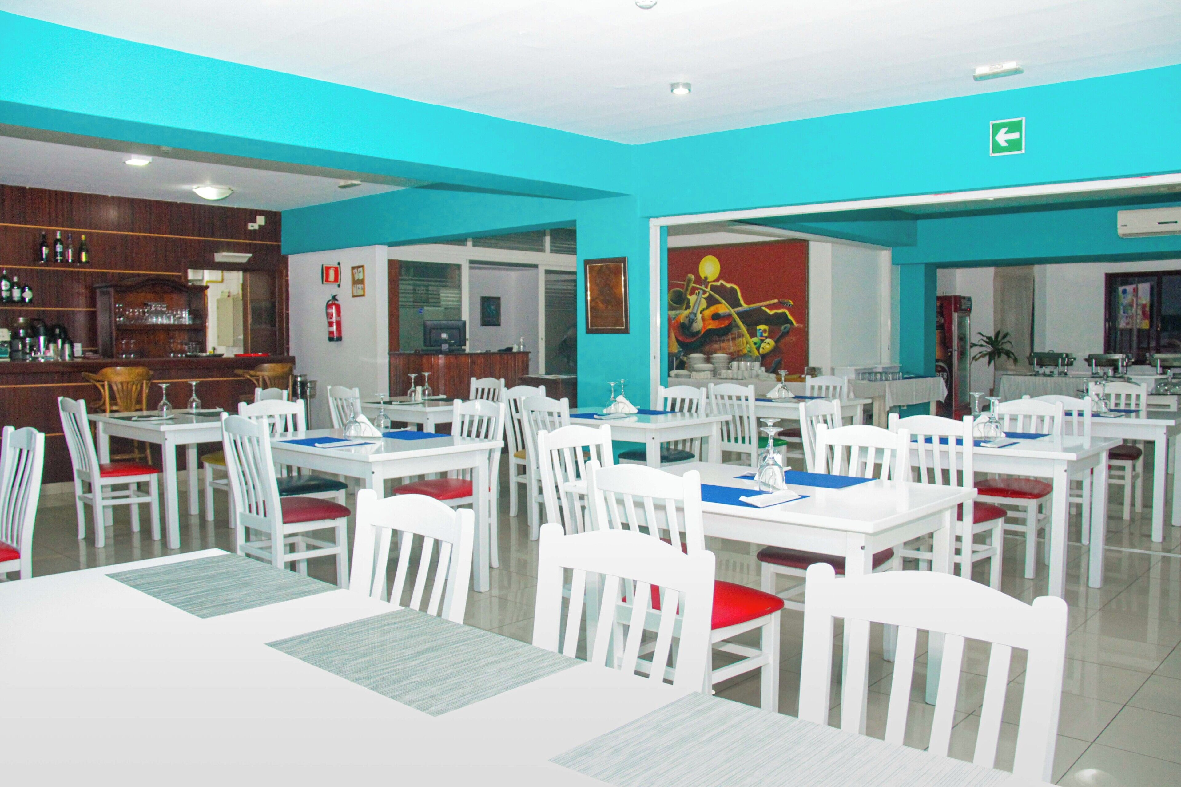 A restaurant with white tables and chairs, a bar area, and a mural on the wall.