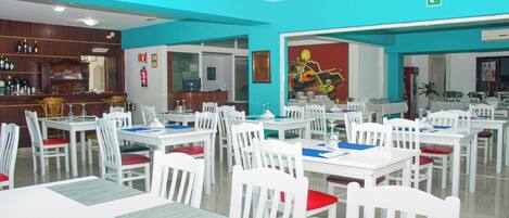 A restaurant with white tables and chairs, a bar area, and a mural on the wall.