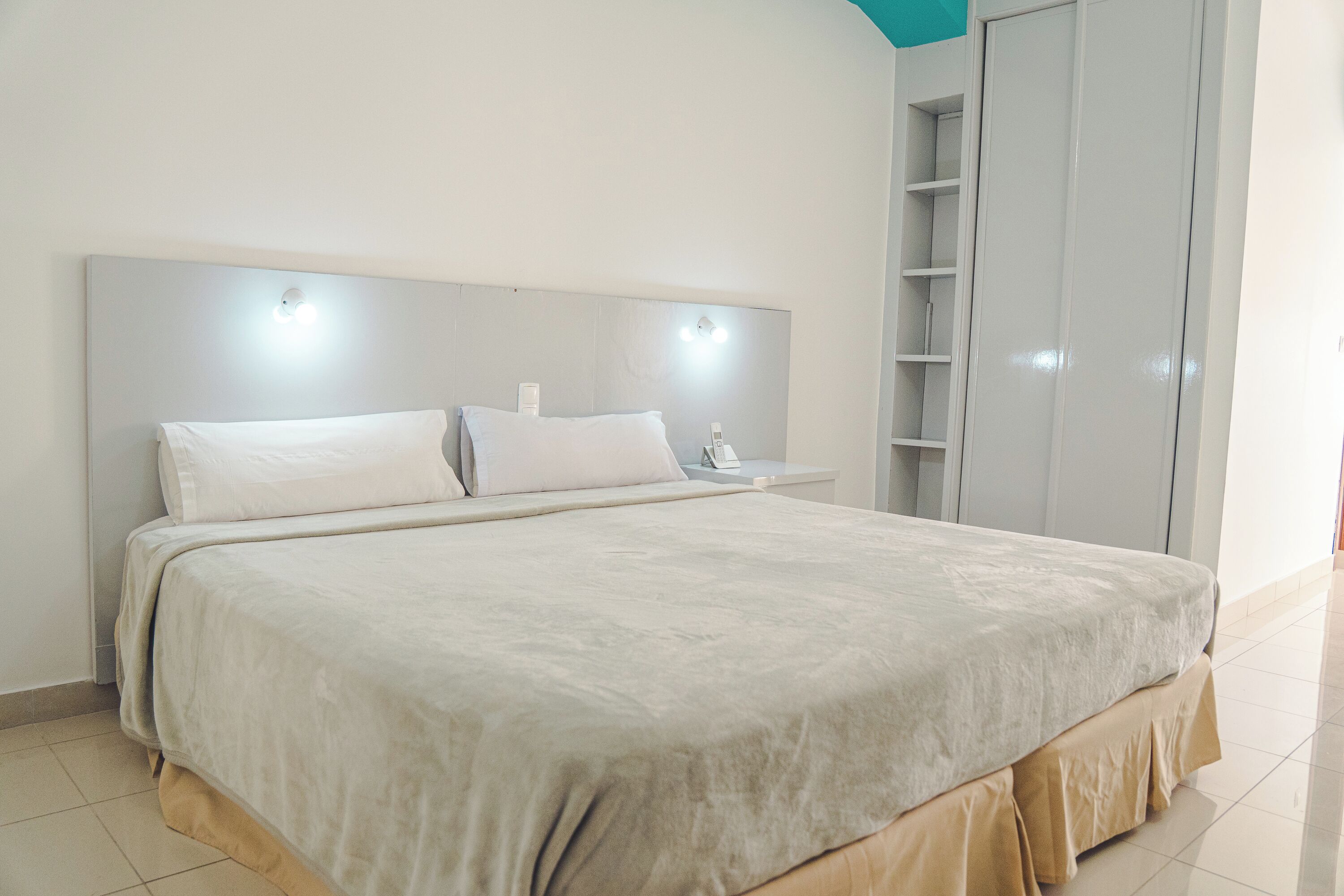 Een groot bed met hoofdeinde, nachtkastje en kledingkast.