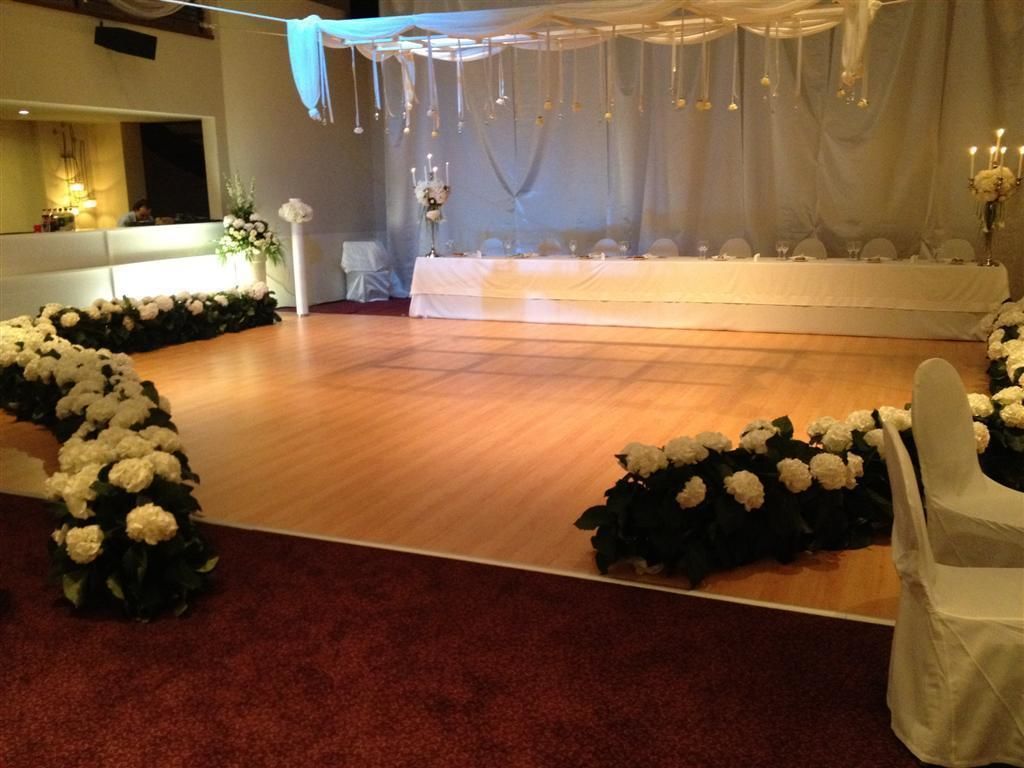 An indoor event space with a stage, white floral arrangements, and a red carpet.
