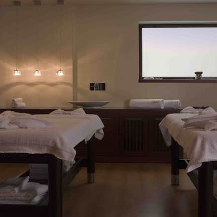A spa room with two treatment tables, a large window, and a view of the sky.