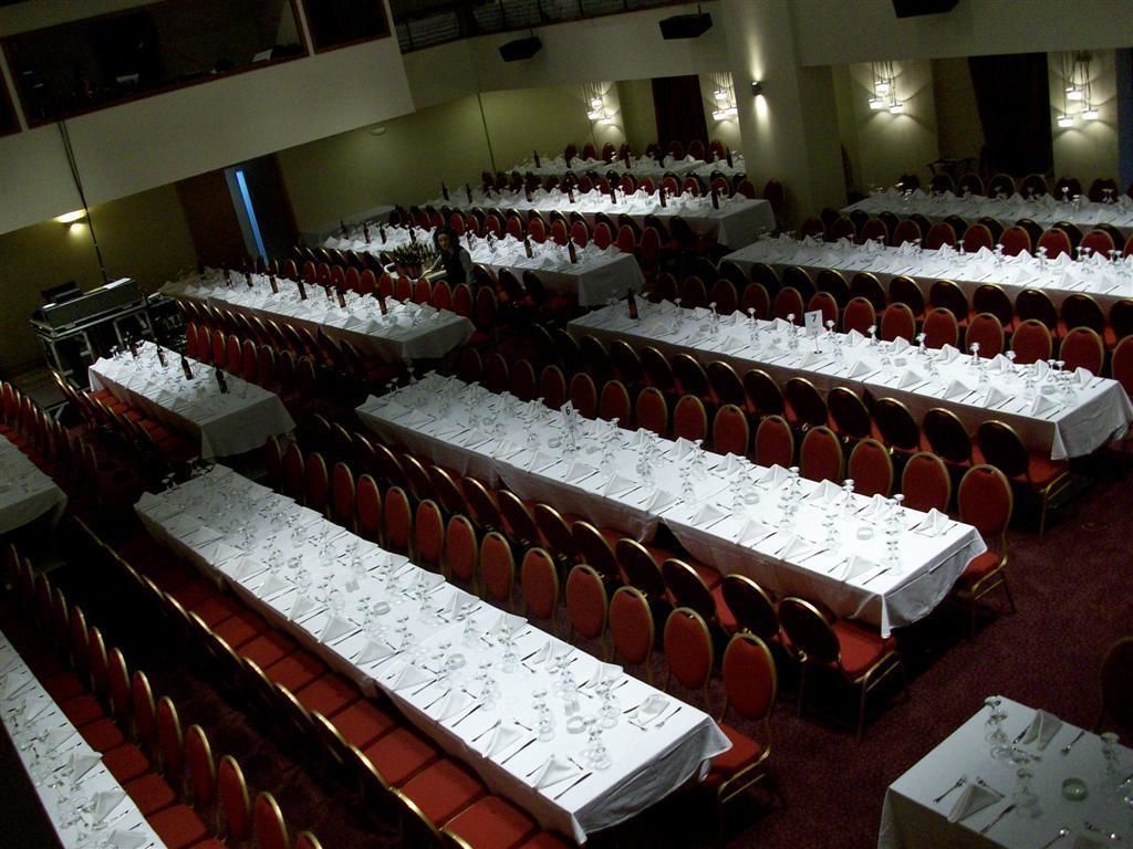 A conference room with multiple tables set for dining, arranged in rows with red chairs.