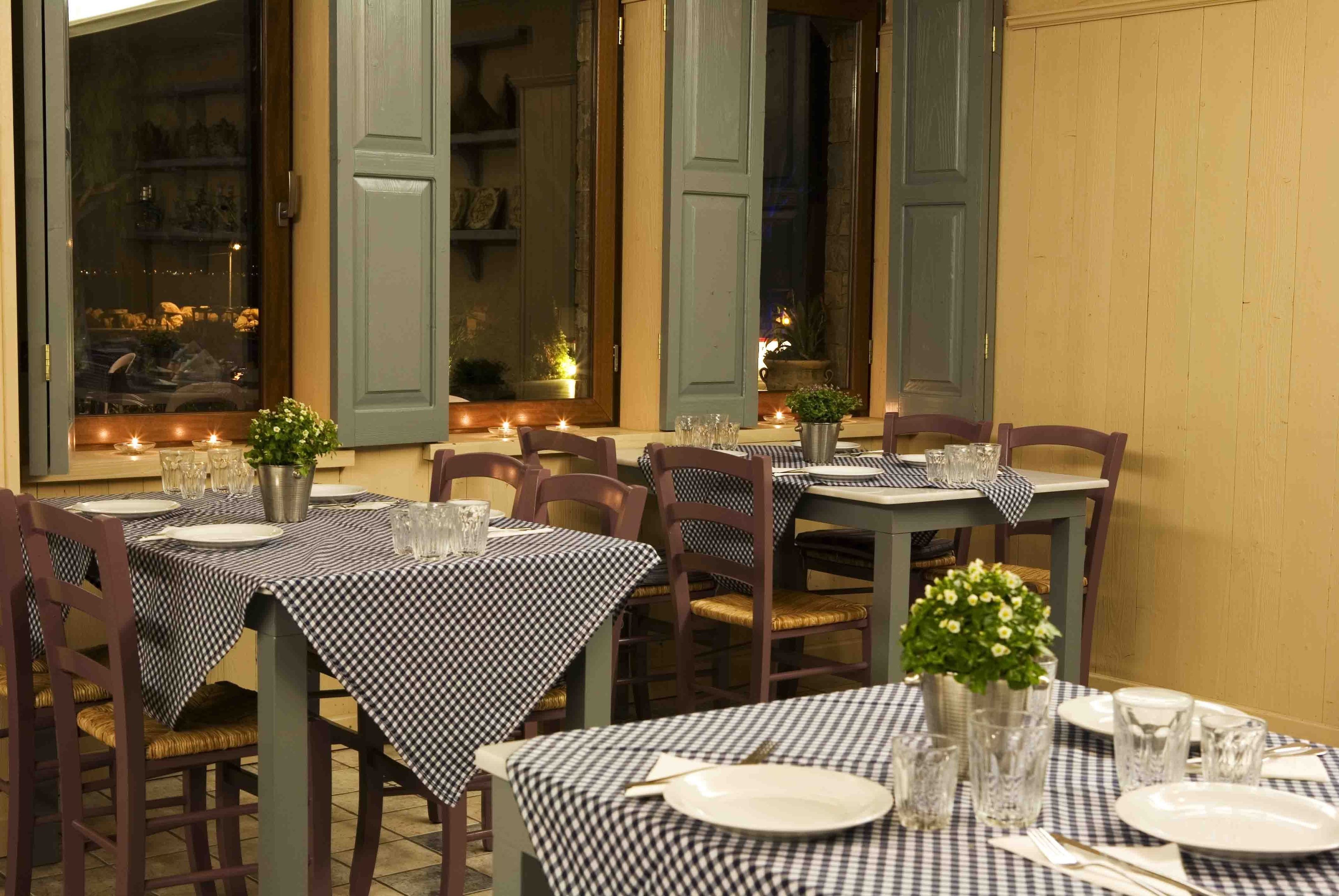 Un comedor con manteles a cuadros, sillas de madera y plantas en macetas.