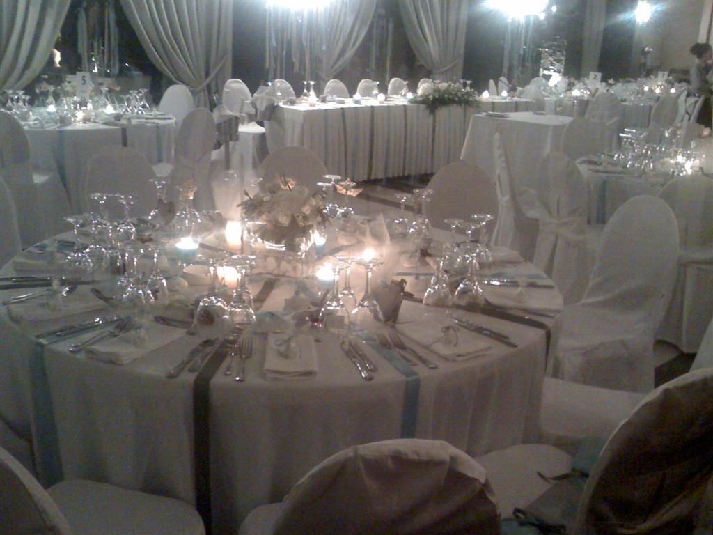 Un salón de banquetes con mesas redondas preparadas para un evento formal, cada una decorada con manteles blancos y velas.