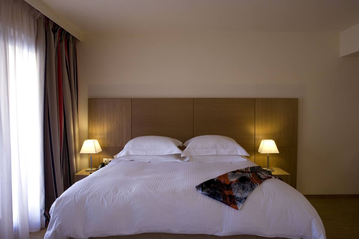 A hotel room with a large bed, two bedside lamps, and a headboard.