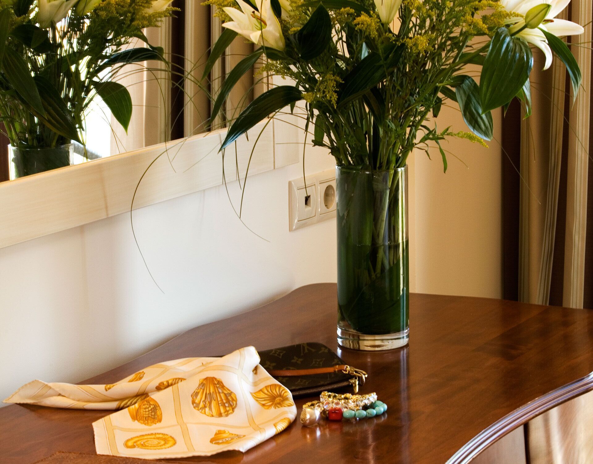 A wooden table with a vase of flowers, a patterned cloth, and a small bag of keys.