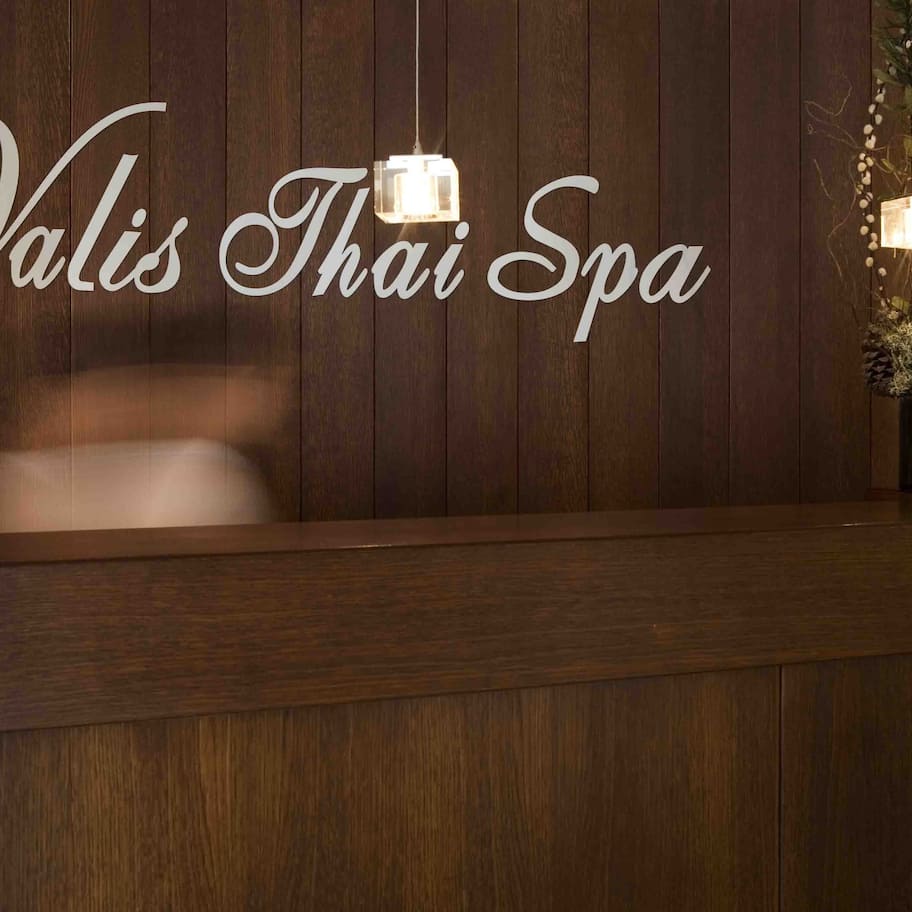 A reception desk with a wooden panel background and a sign reading "Valis Thai Spa".