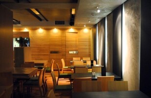 Un interior de restaurante moderno con paredes de madera, varias mesas y sillas, y un letrero que indica el baño.