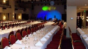 A banquet hall with rows of tables set for a formal event, equipped with wine glasses and white tablecloths.