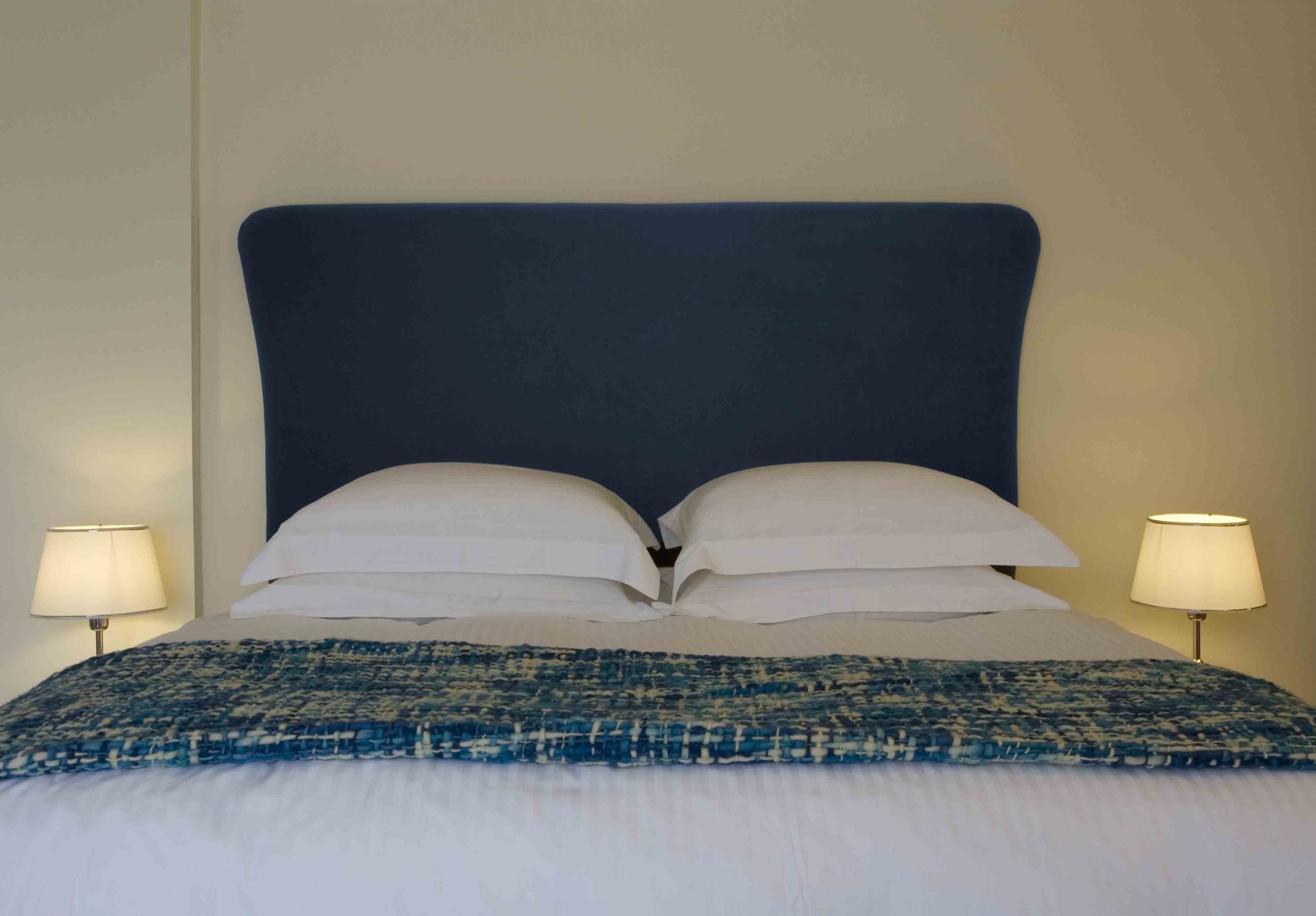 Cama bem arrumada com cabeceira escura, almofadas brancas e edredom azul estampado.