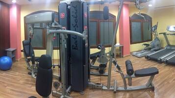 Ein Fitnessstudio mit verschiedenen Trainingsgeräten, darunter eine Langhantelbank, ein Rudergerät und ein Laufband.