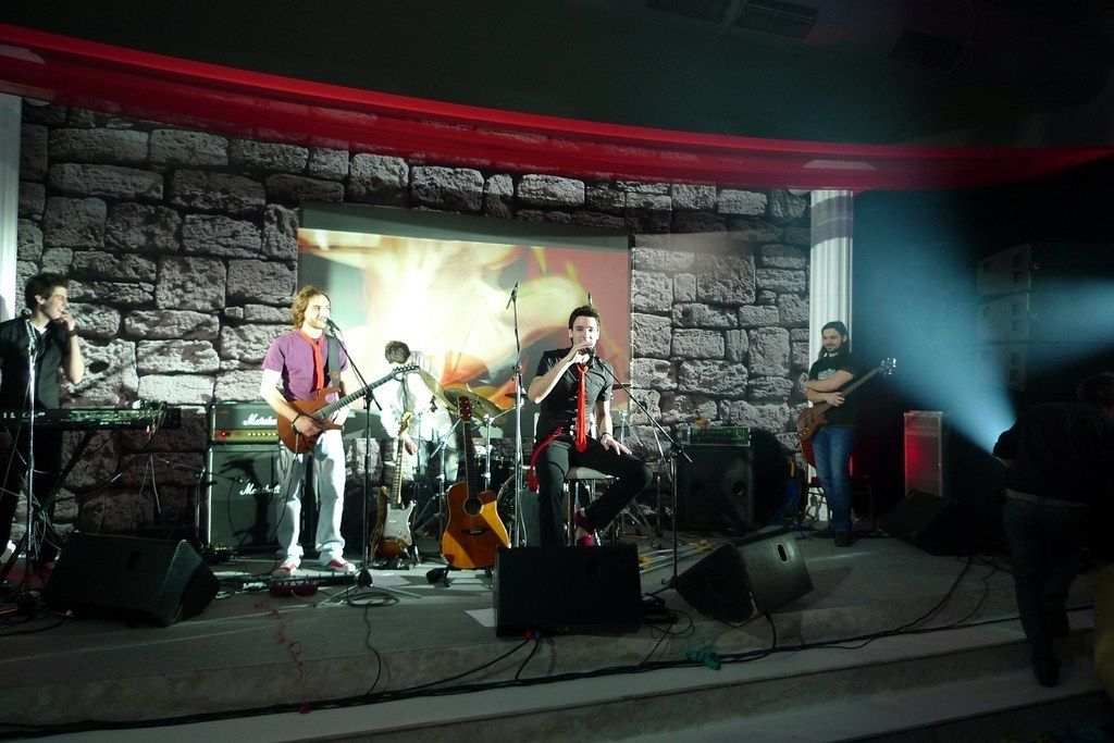 A band performing on a stage with a stone wall backdrop and a red curtain.