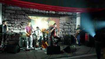 A band performing on a stage with a stone wall backdrop and a red curtain.
