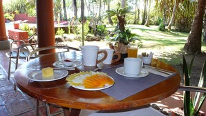 Una mesa de madera preparada para el desayuno, con platos, tazas y una bandeja de fruta.