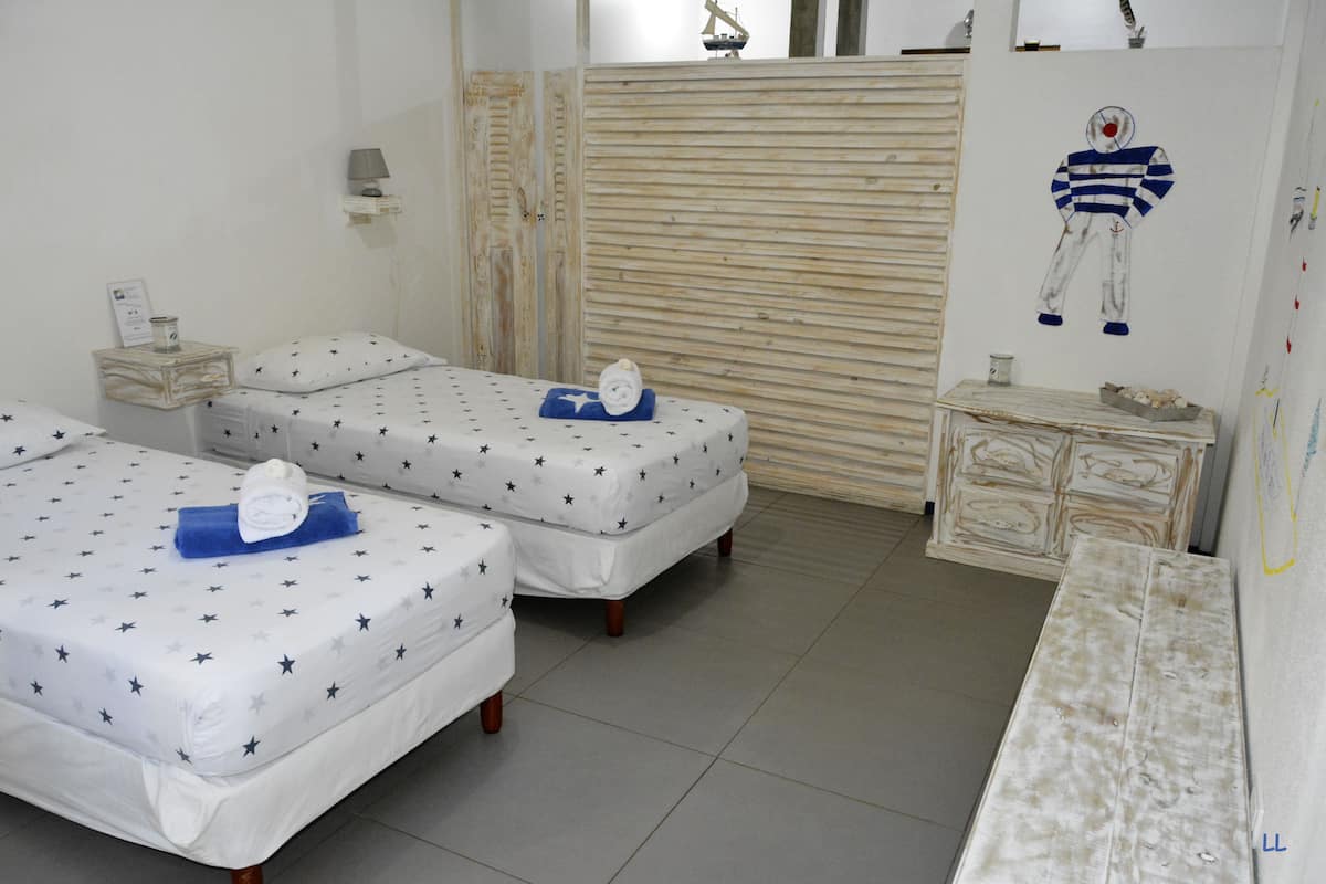 A room with two beds, each with star-patterned bedding, a small bedside table with a lamp, and a wall-mounted artwork.
