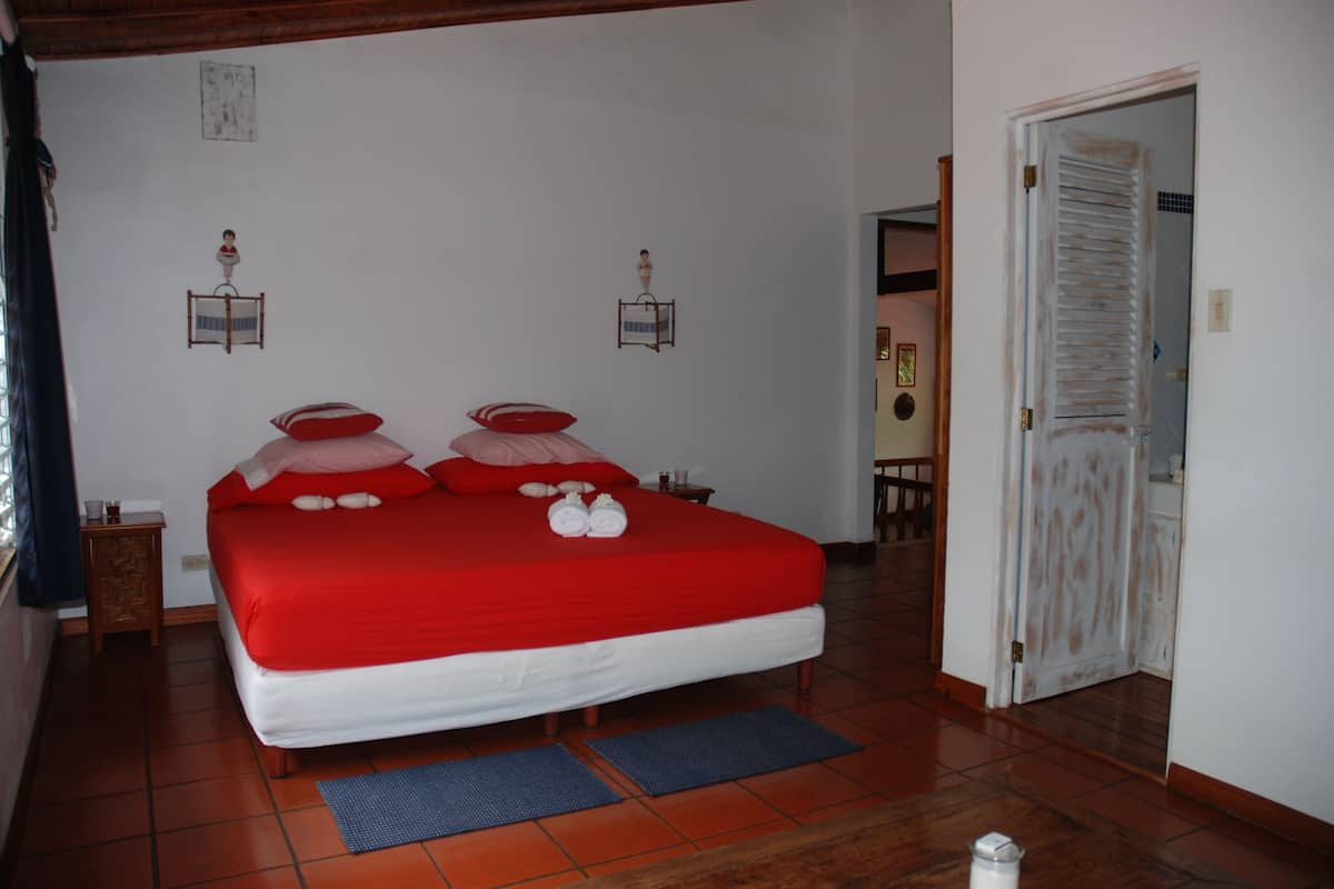 A neatly made bed with red bedding, a wooden headboard, and two wall-mounted lamps.
