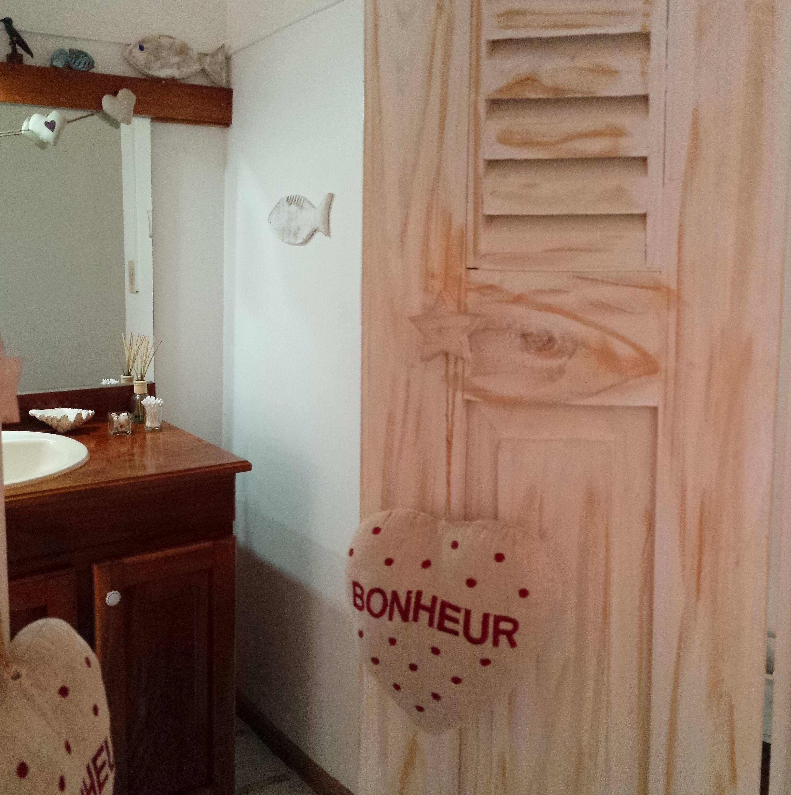 Une salle de bain avec un meuble-lavabo en bois, un miroir, un porte-serviettes avec une serviette et une décoration murale représentant un poisson.