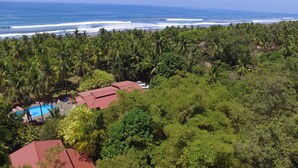 Un resort con varias edificaciones de techo rojo rodeado de exuberante vegetación tropical y una playa con olas.