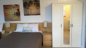A hotel room with a bed, a wardrobe, a nightstand, a lamp, and two wall-mounted paintings. - Breakaway Inn (Lauderdale-by-the-Sea)