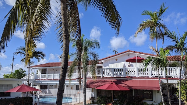 A two-story building with a white exterior and red roof, surrounded by palm trees and a swimming pool. - Breakaway Inn (Lauderdale-by-the-Sea)