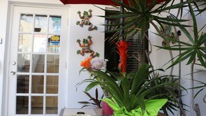 A door with frosted glass panels, a small table with a bowl of fruit, and various potted plants. - Breakaway Inn (Lauderdale-by-the-Sea)