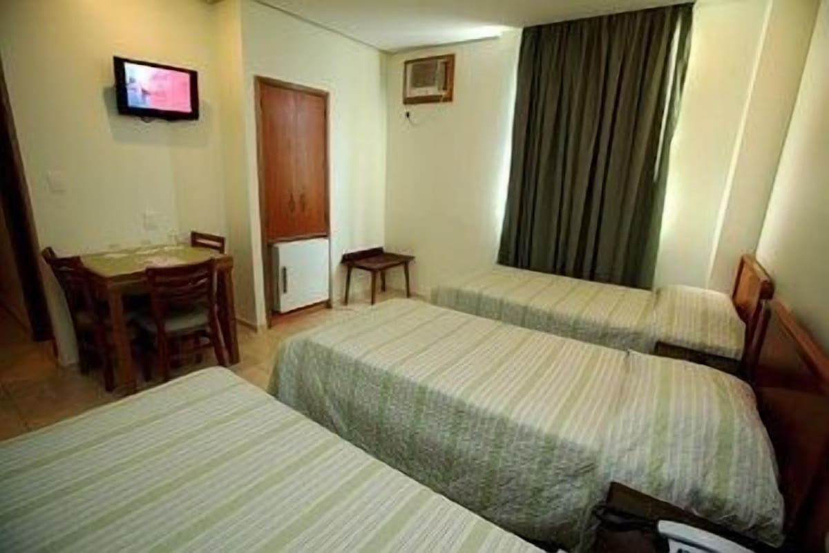 Une chambre d’hôtel avec deux lits simples, un petit bureau avec une chaise, une télévision et une porte.