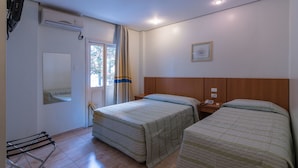 Habitación de hotel con dos camas, televisión, aire acondicionado, espejo, un cuadro enmarco y una ventana con cortinas.
