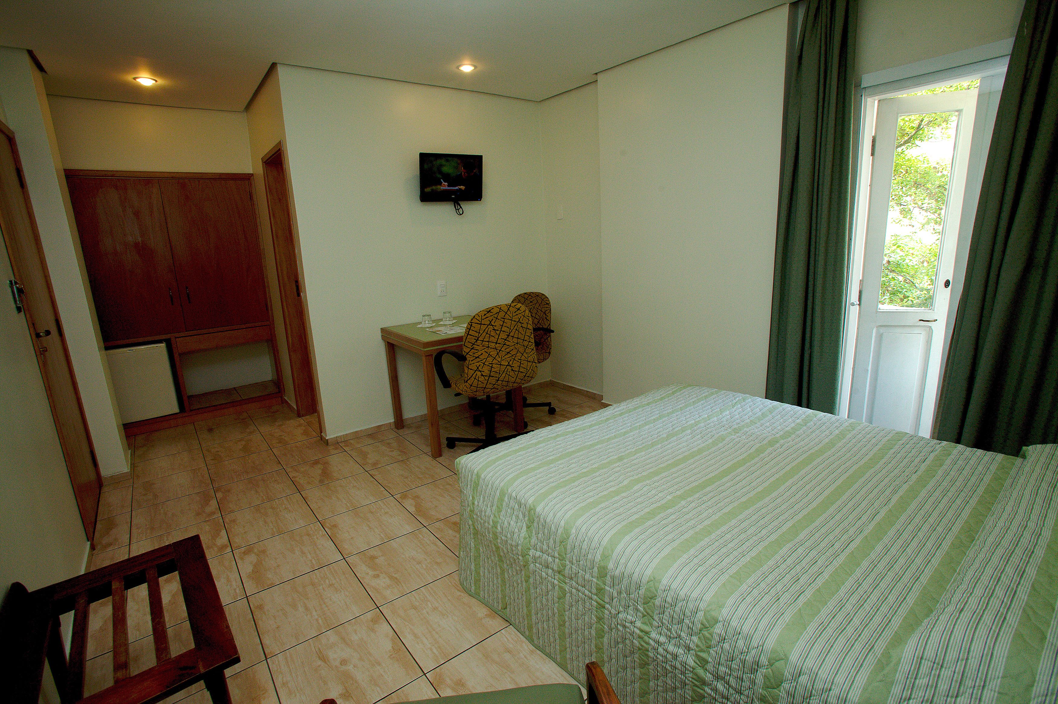 Un dormitorio con cama, escritorio, silla y televisión en la pared.