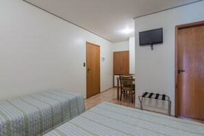 Una habitación con dos camas, una puerta de madera, un televisor, una mesita con una silla y un perchero metálico.