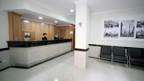 Zona de recepción con mostrador, recepcionista y área de descanso con sillas.
