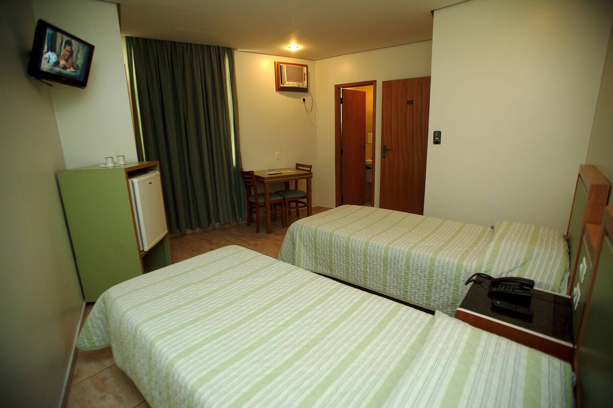 Une chambre d’hôtel avec deux lits simples, un petit bureau avec une chaise, une télévision et un réfrigérateur.