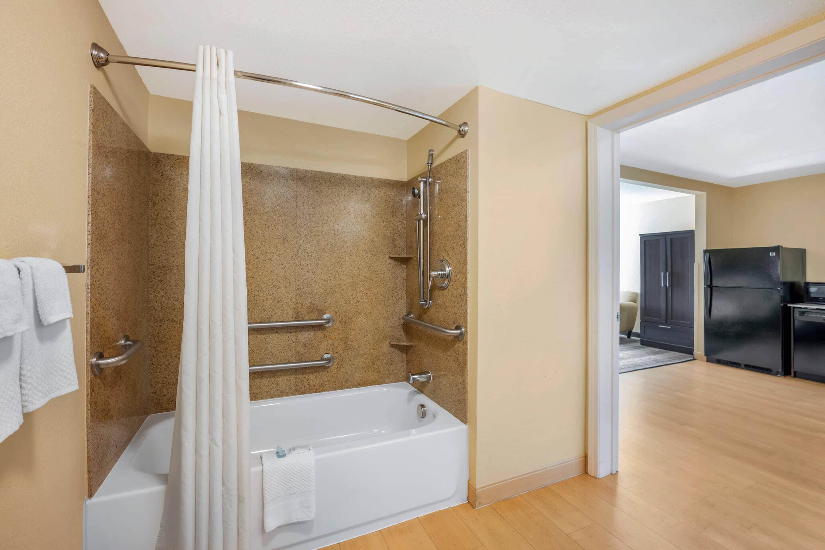 A modern bathroom with a bathtub, shower, and grab bars.
