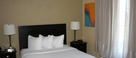 Una habitación de hotel con una cama, dos mesitas de noche, un armario de noche, un aire acondicionado instalado en la pared y una ventana con cortinas.