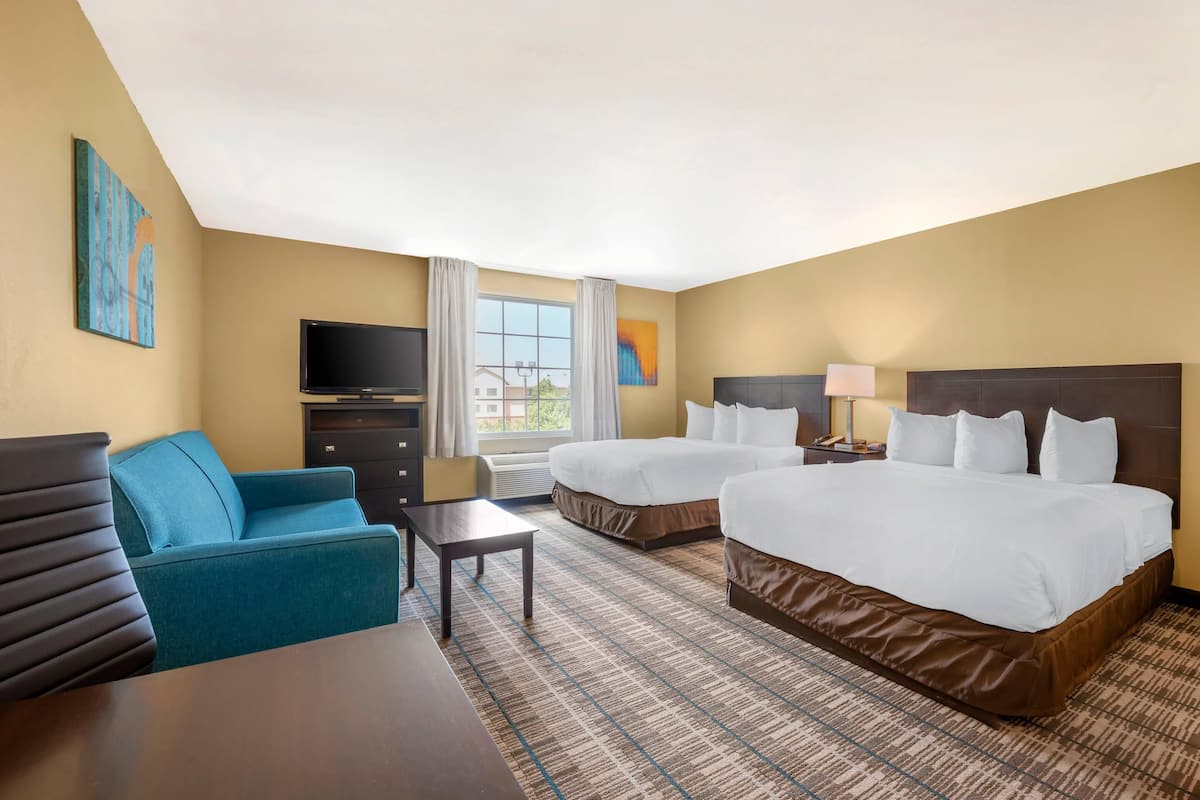 A hotel room with two beds, a TV, a desk, and a couch.