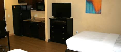A hotel room with a bed, a TV, a kitchen area, and a painting on the wall.