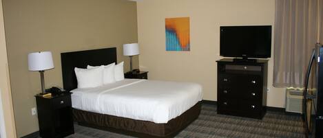 A hotel room with a large bed, two bedside tables with lamps, a flat-screen TV, a dresser, and a carpeted floor.