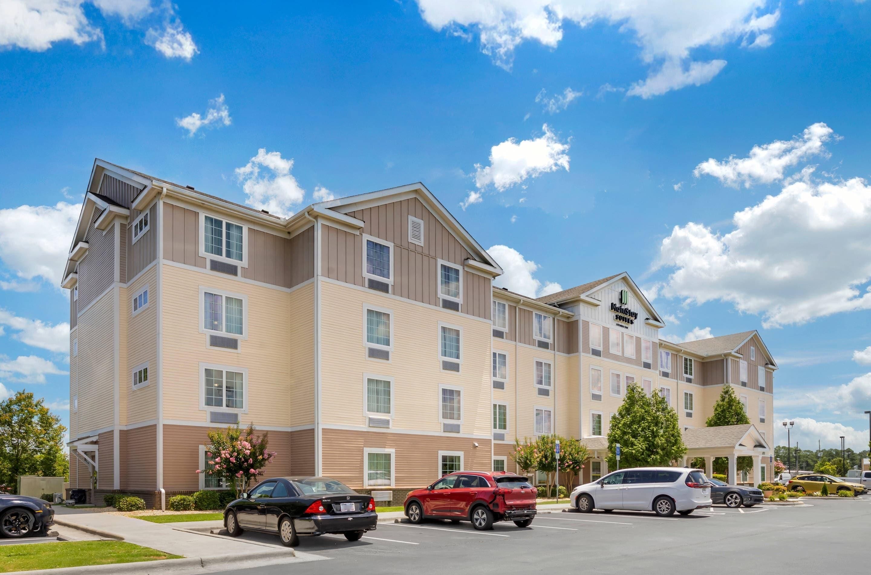 A multi-story hotel with a modern design, featuring a parking lot with several cars.