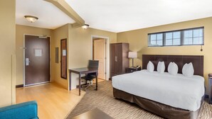 Habitación de hotel con una cama grande, un escritorio, una silla, un armario y una ventana con persianas.