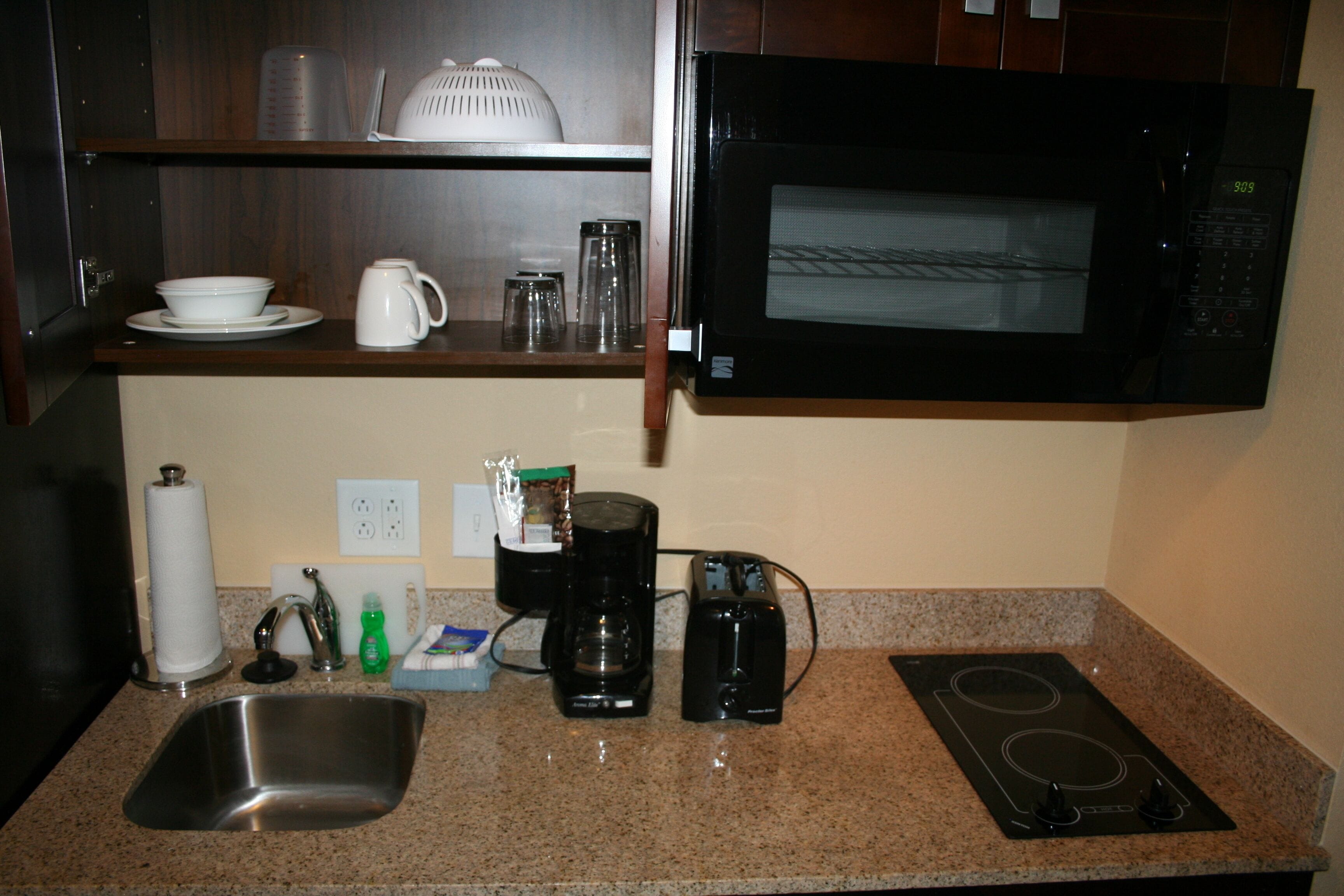 A kitchen with a stainless steel sink, a coffee maker, a microwave, and a stovetop.