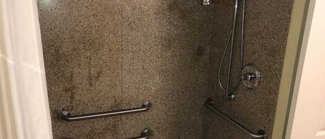 A bathroom with a white bathtub, granite walls, and a shower with a handheld showerhead.