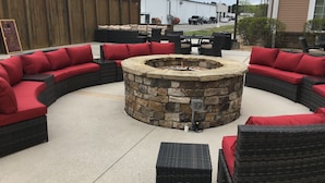 Un espacio de estar al aire libre, circular, con una chimenea de piedra rodeada de muebles de mimbre con cojines rojos.