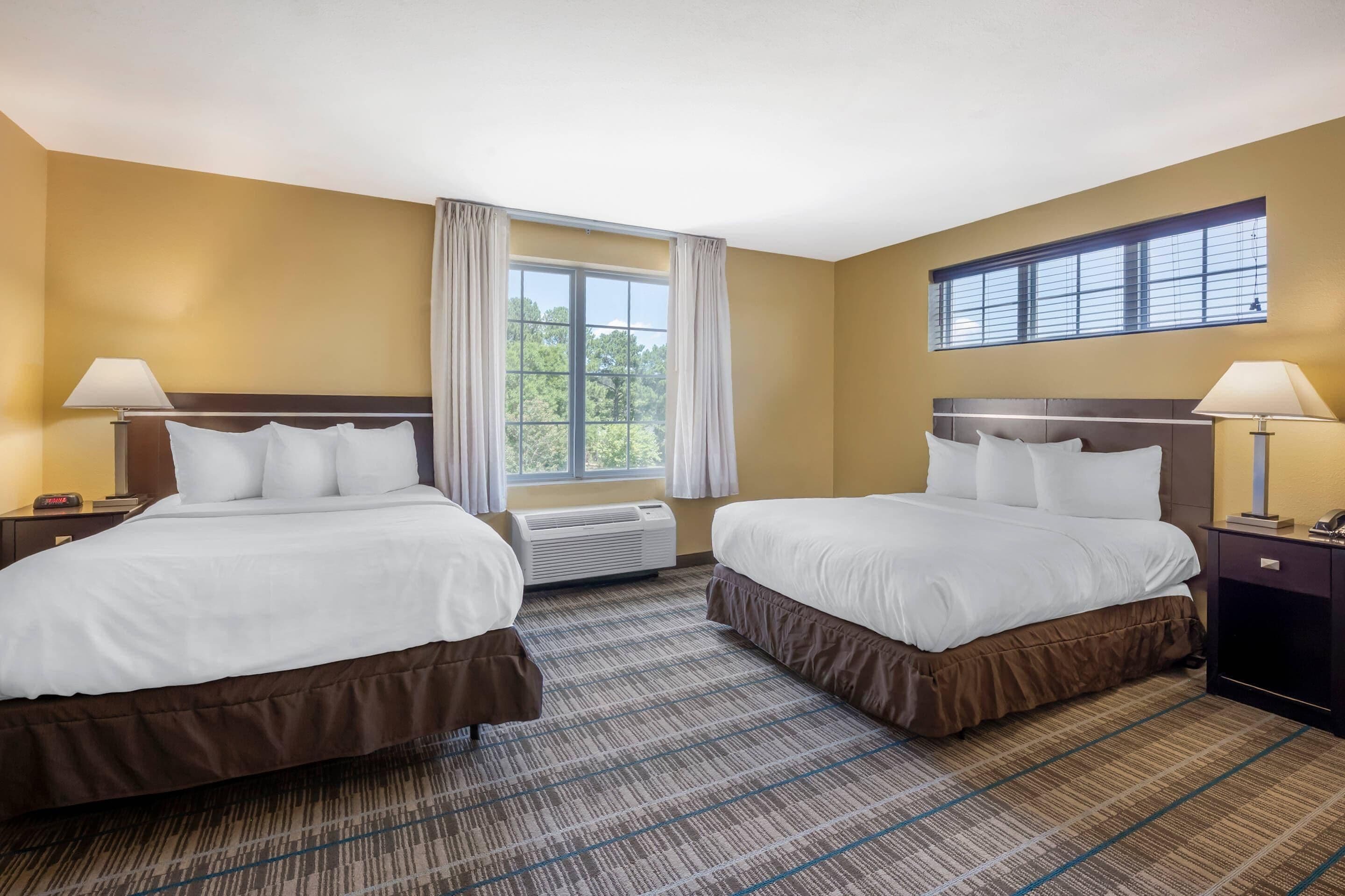 Habitación de hotel con dos camas, un ventanal con cortinas, un equipo de aire acondicionado y vistas a zonas verdes.
