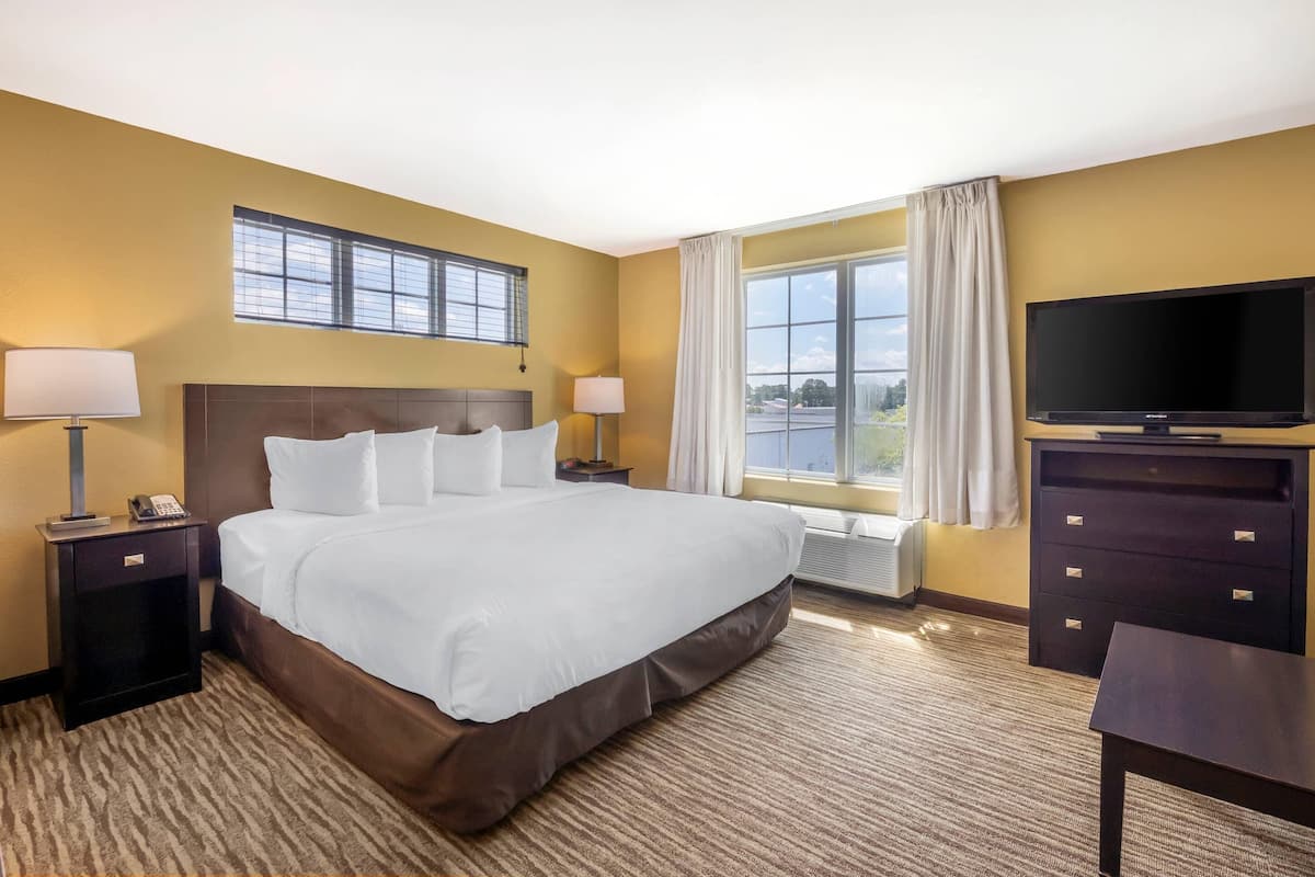 A hotel room with a large bed, two bedside tables with lamps, a TV, and a window with curtains.