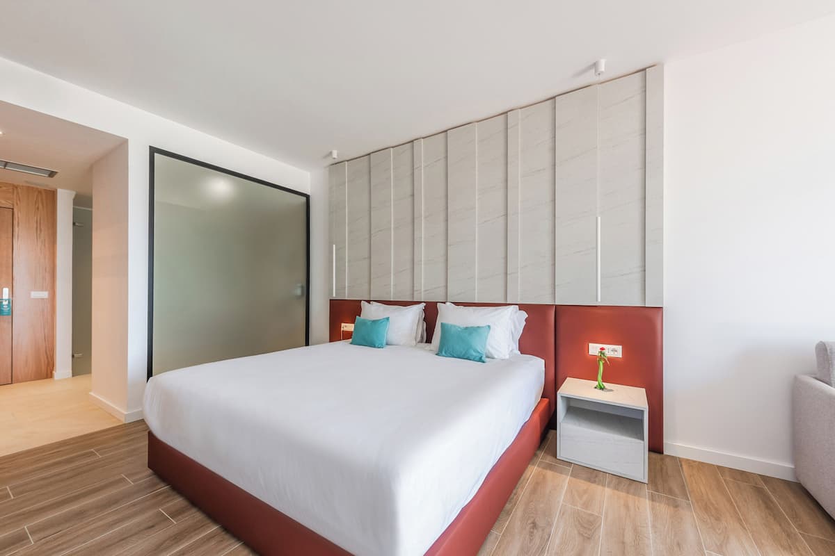 A modern hotel room with a large bed, a nightstand, a red headboard, and a sliding door closet.