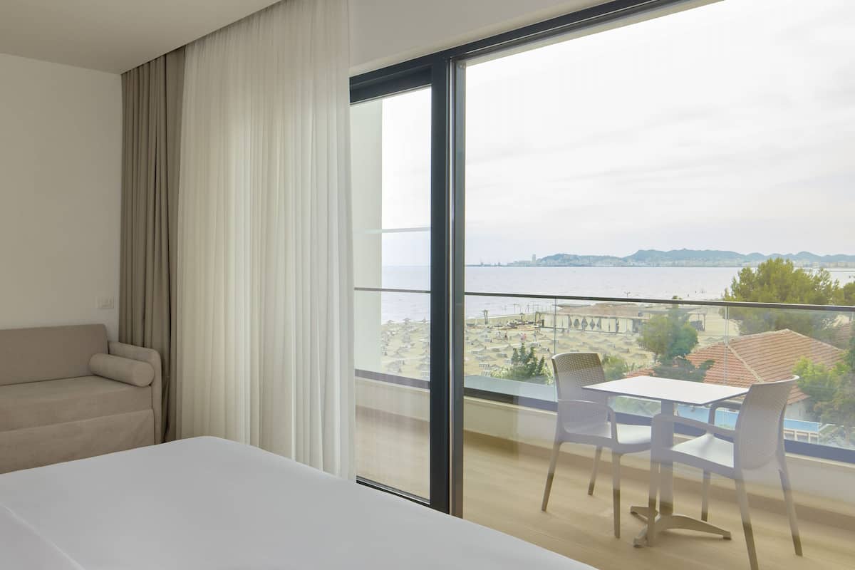 A hotel room with a large window, a bed, a sofa, and a balcony with a table and chairs.