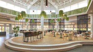 Un amplio comedor interior con varias mesas y sillas, una zona de estar central y plantas colgantes.